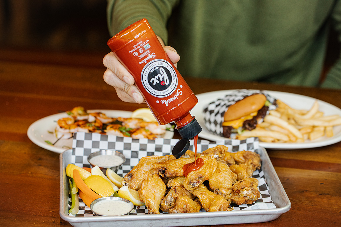 Fix Signature Sriracha Hot Sauce being poured on chicken wings.